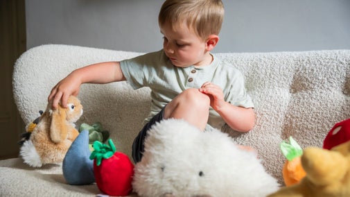 A toddler sat on a sifa playing with soft toys